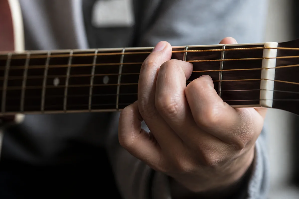 Mains d’un musicien sur un manche de guitare, lumière naturelle de fenêtre